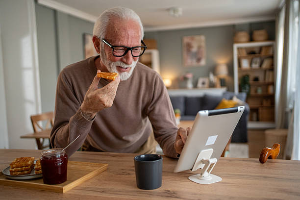 istock Senior man enjoying breakfast and browsing internet on tablet at home 2219055209