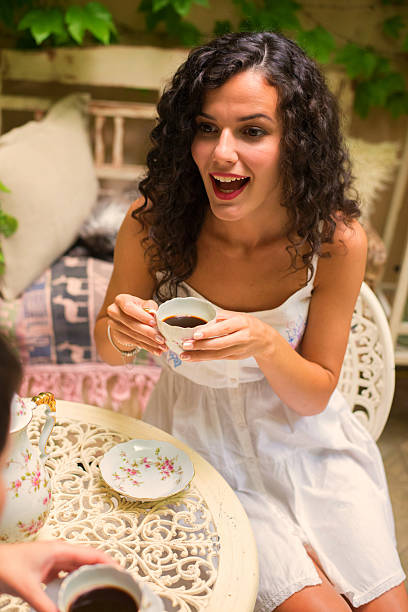 Two smiling young women talking and drinking coffee  in the back yard in summer.