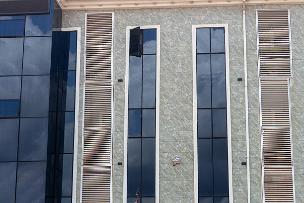 The detailed facade of a modern commercial building, featuring stone tile cladding, tall windows, and vertical louvered vents for ventilation or screening.
