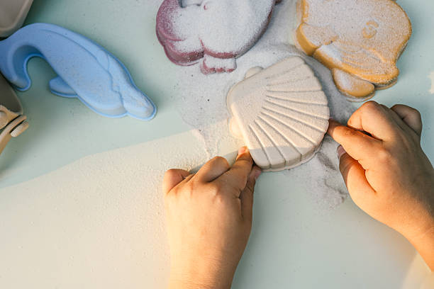 istock Child playing with pastel beach toys shaped like sea animals and shells, arranged on a light surface with scattered sand. A beige bucket and scoop add to the soft, summery, and educational setting 2219064206