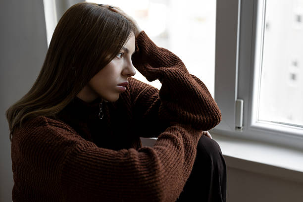 istock Depressed woman looking through window 2219075534
