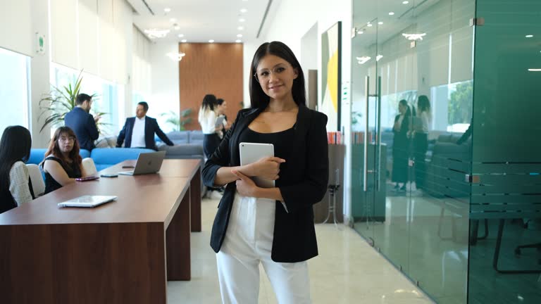 Office worker posing facing forward with a computer in her hands dressed elegantly