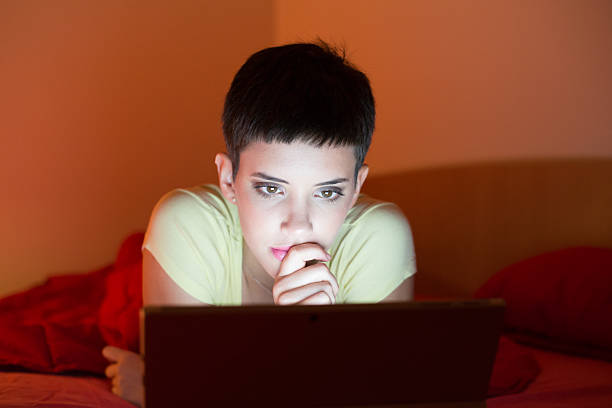 Young woman using laptop while lying in bed at night.