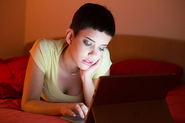 Young woman using laptop while lying in bed at night.