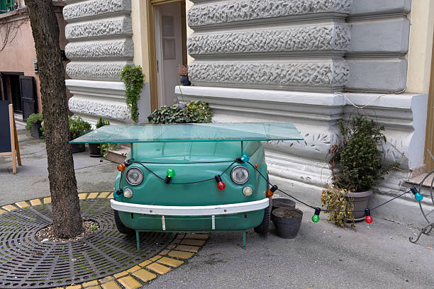A creative outdoor table repurposed from the front of a vintage green car, topped with a glass sheet and decorated with colorful string lights.