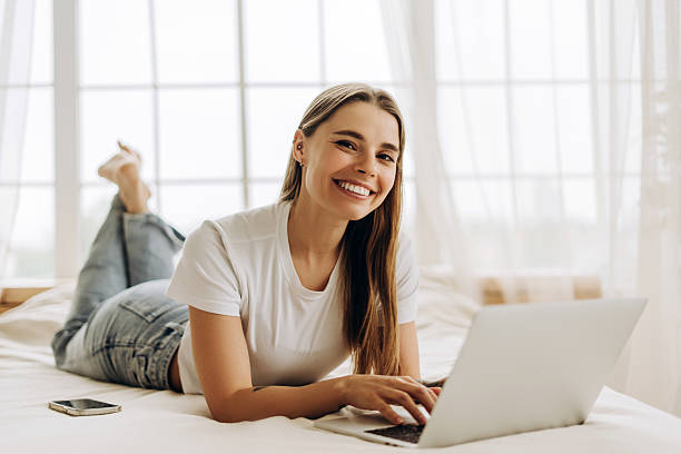 istock Smiling woman lying on bed using laptop and working remotely from home 2219081688