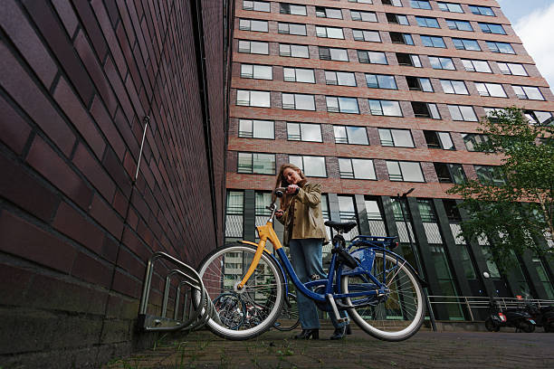 Young woman securing her bicycle to a parking rack in front of a contemporary brick building, enjoying urban commuting and active lifestyle