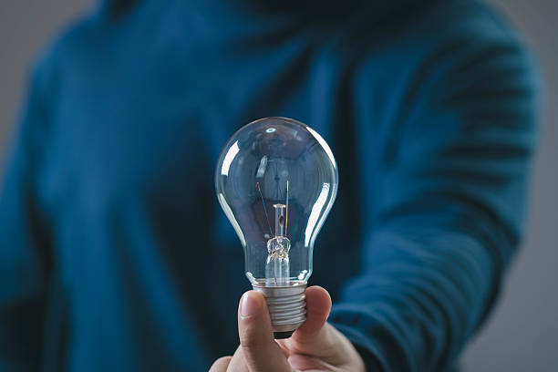 istock Hand holding a light bulb symbolizing innovation and bright ideas on a gray background. Person in blue sweater emphasizing simplicity and focus. 2219101266