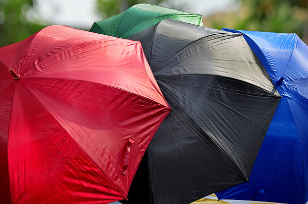 four open umbrellas in red, black, blue and green with blurry fresh tree background outdoors