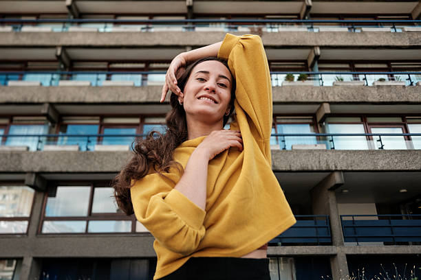 istock Young woman posing with yellow sweatshirt in front of brutalist architecture 2219111232