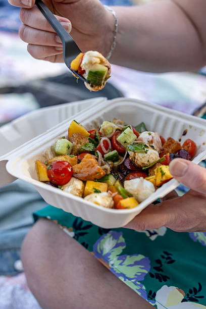 istock Woman's hand holding a bite of a summer salad with fruit cheese and crispy bread with dressing on a summer evening at an event on a blanket. 2219115196