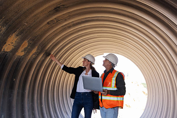 istock Two engineers wearing safety helmets and vests review construction plans on a laptop inside a large corrugated pipe 2219116792
