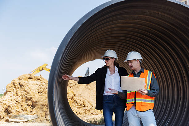 istock Two construction professionals with safety helmets discuss site plans near a large drainage pipe at an urban construction site 2219116795