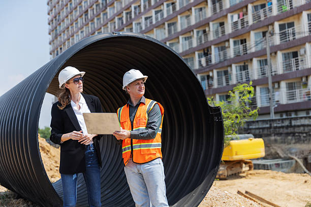 istock Two construction professionals with safety helmets discuss site plans near a large drainage pipe at an urban construction site 2219116797