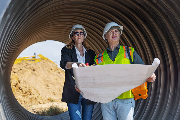Two engineers in safety gear stand inside a large corrugated pipe at a construction site