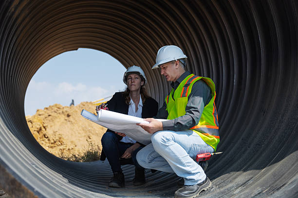 istock Two construction professionals in safety gear crouch inside a large drainage pipe 2219116862