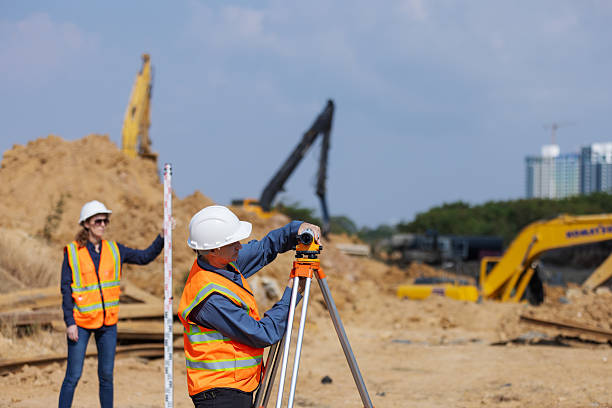 istock Two construction surveyors in safety gear perform land measurement at a worksite using a total station and leveling rod, 2219116929