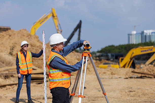 istock Two construction surveyors in safety gear perform land measurement at a worksite using a total station and leveling rod, 2219116932
