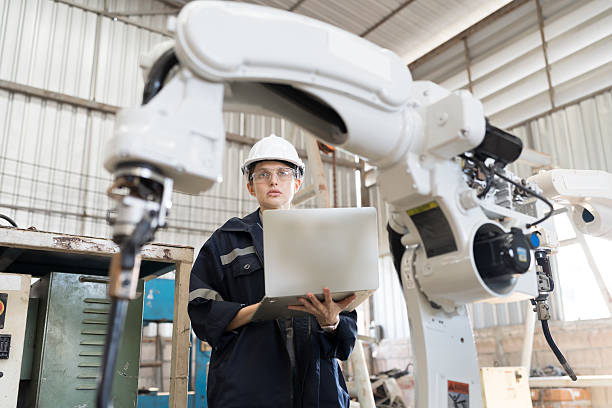 istock Robotic arm, Robotic manufacturing industry. Woman engineer working with laptop computer for setup, install, maintain, repair mechanism of operation of robotic arm in workshop 2219117369