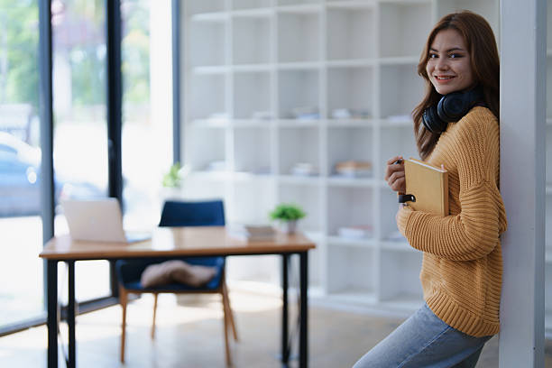 istock Smiling student leans against pillar in study room with a book and headphones. 2219118072