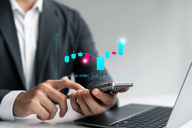 istock Businessman analyzing candlestick chart on smartphone with laptop, representing stock trading, financial analysis, cryptocurrency investment, data visualization, and market trends. 2219123103