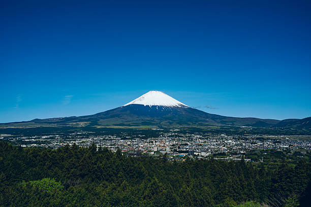 Snow-capped Mt. Fuji with a city spread at its base, full view