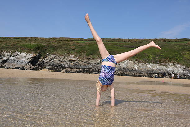 Young blonde haired girl doing cartwheel in shallow water on a sunny day