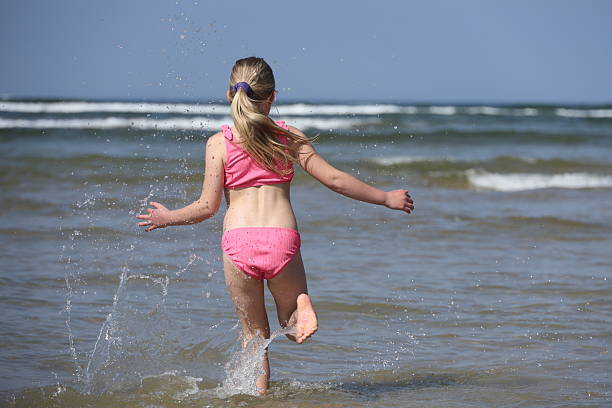 Young blonde haired girl running into the sea wearing a pink bikini on a beach holiday