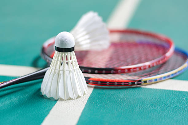 Badminton sport equipments, rackets and shuttlecocks, on badminton floor of indoor court, soft focus.