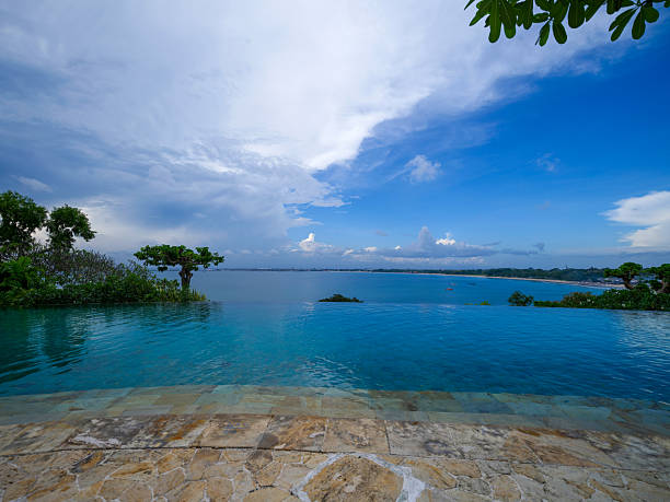 wooden sunlounger chairs near a swimming pool with blue water with sea and a small island in the background at sunset