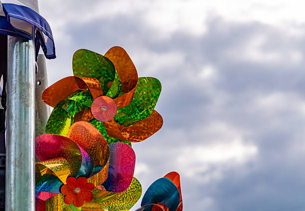 Colorful foil pinwheels placed by a metal pole against a cloudy sky background.