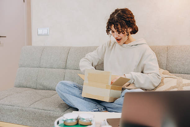 istock Young woman opening a package sitting on the sofa at home 2219141536