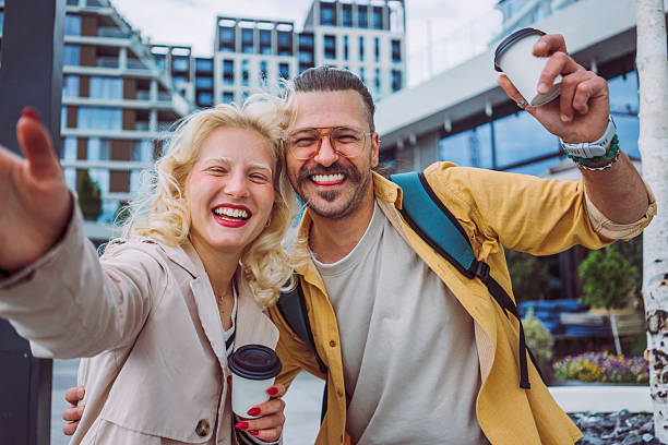 istock A young couple takes a selfie while walking and holding takeaway coffee cups, enjoying a casual moment together in an urban setting. Captures a candid and affectionate scene of modern city life 2219143213