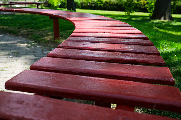 A bright red bench curves gracefully in a lush green park under clear skies.