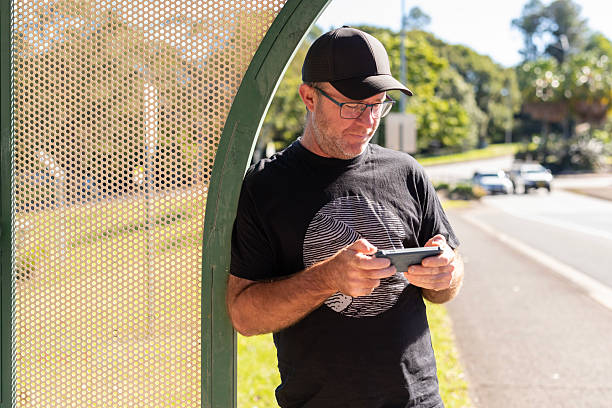 Middle aged man mobile phone gaming waiting for a bus
