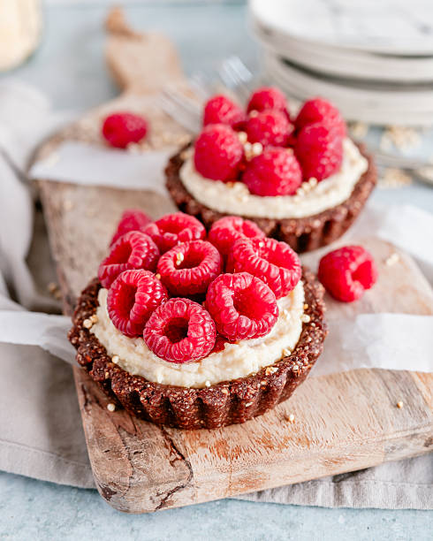 Close-up of two healthy vegan no-bake tartlets with cashew cream and fresh raspberries