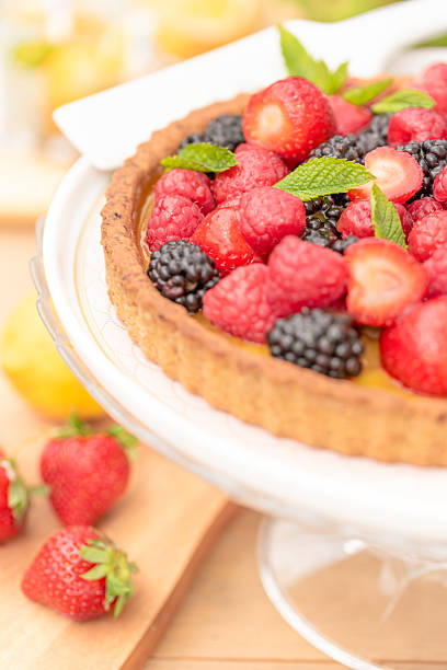 Homemade summer berry tart made with a sweet buttery french crust, a lemony cream filling and topped with fresh fruit topper and apricot glaze on a footed cake platter, a classic french tarte