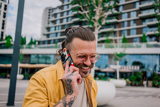 istock A young man smiling while talking on a smartphone and holding a laptop, seated on a bench in a modern urban area. 2219150437