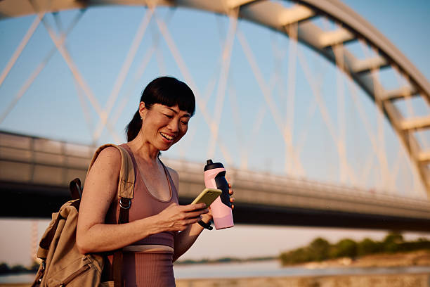 istock Sporty woman using smartphone and holding water bottle under bridge 2219154962