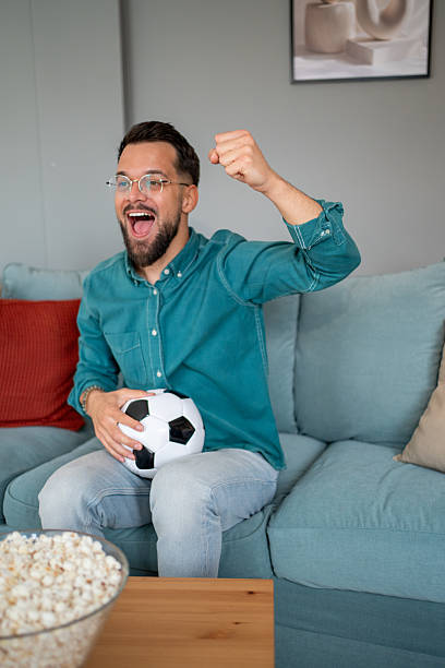 istock Excited soccer fan celebrating goal while watching match at home 2219155495