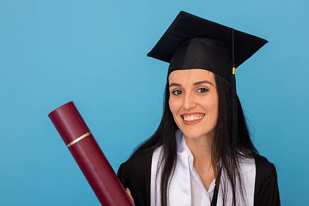 istock Young graduate wearing black gown, beaming with pride while holding diploma and posing confidently against blurred background 2219158074