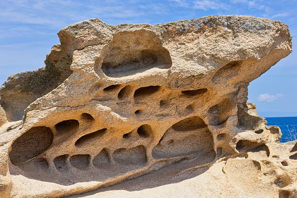 A porous rock formation sits on a sandy surface under a blue sky on Diaporos Island - Sithonia - Chalkidiki - Macedonia - Greece