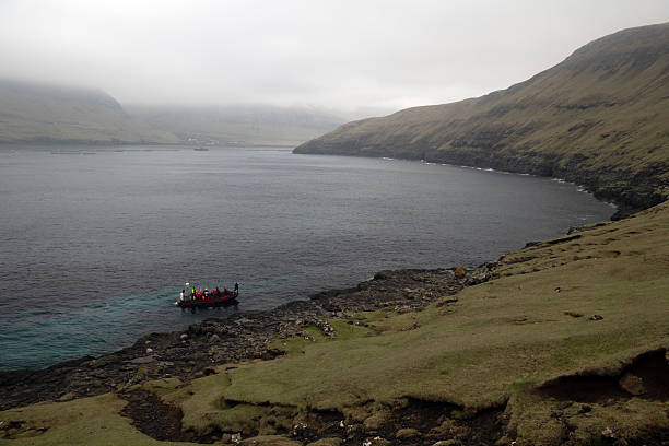 Tourists leaving Drangarnir in open boat. No recognizable people. Faroese seascape on a cloudy day.
