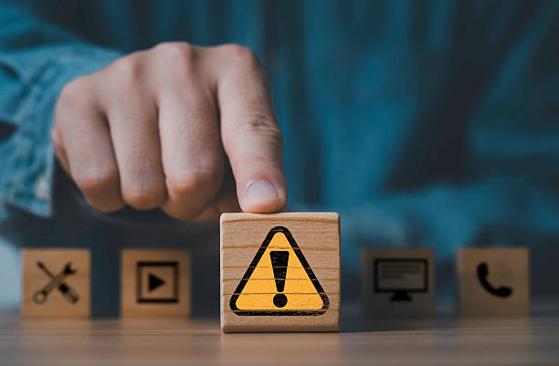 istock Businessman posing  yellow triangle caution warning sign in front of technology icon  for notification error and maintenance concept. 2219166877