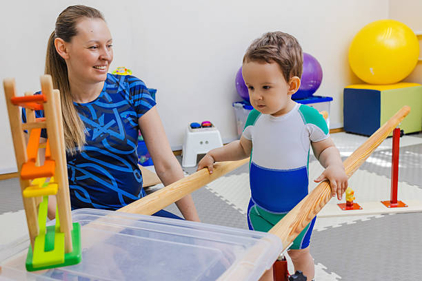 istock Little male child is engaging in physical therapy, assisted by a caregiver, using parallel bars to improve mobility. Handrails for restoring walking skills for children 2219170712
