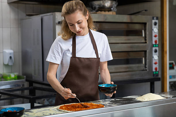 istock Female cooker putting filling into pizza in the kitchen 2219182016