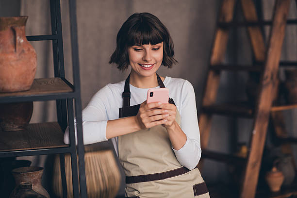 istock Photo of professional lady potter use smart device chatting client making present porcelain product vase in workroom 2219185925