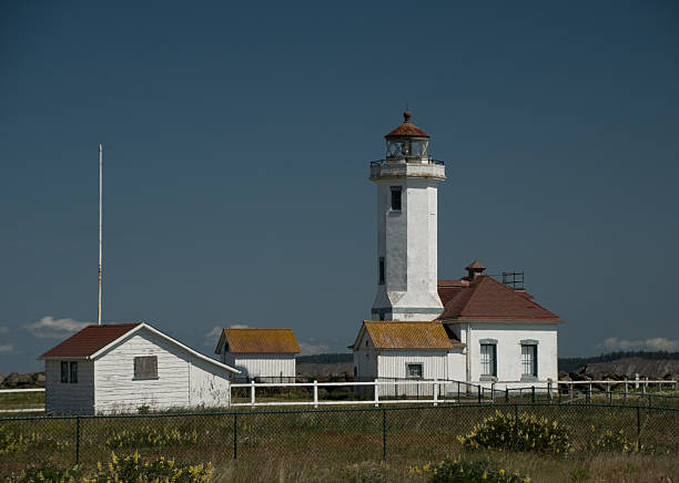 Point Wilson Lighthouse surrounded by grass field and mesh fence, Fort Worden, Port Townsend