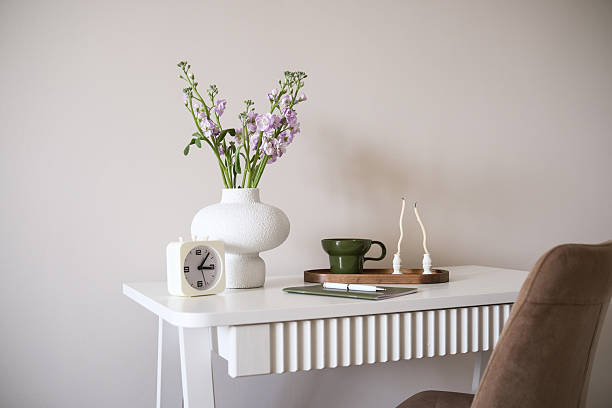 istock A stylish white desk meticulously arranged with flowers, a clock, and elegant minimalist decor elements - cup of coffee, notebook, candles, pen. 2219192821