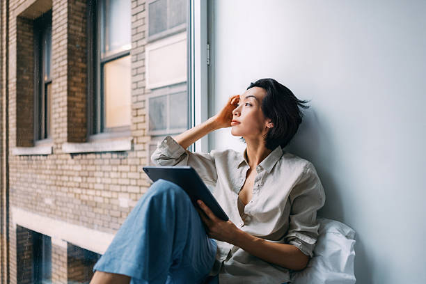 Thoughtful Woman Relaxing by Window with Tablet in Urban Setting